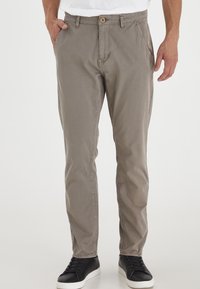 Grå chinos laget av myk bomull med avslappet passform, med knappelukking og sidelommer. Kombinert med svarte sneakers.