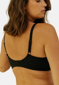 Soutien-gorge noir avec des bretelles réglables et une fermeture au dos. Tissu lisse avec un minimum de détails, conçu pour un look sans couture.