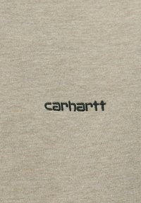 Camiseta de algodón beige con textura acanalada y logo bordado en negro contrastante "carhartt" en el frente.