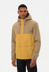 Giacca impermeabile con parte superiore beige e parte inferiore senape, dotata di cappuccio, chiusura con cordoncino e tasche frontali.
