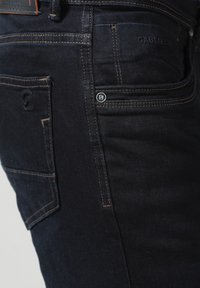 Vaqueros de mezclilla azul oscuro con corte ajustado, costuras prominentes en los bolsillos traseros, un pequeño acento de marca y una textura suave.