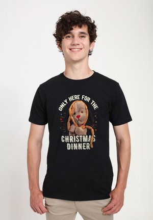 Sort bomulds T-shirt med et grafisk motiv af en tegneseriehund, der holder kager, med teksten "KUN HER FOR JULEFROKOSTEN."