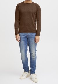 Brązowa koszula z długim rękawem wykonana z wełny, z okrągłym dekoltem i raglanowymi rękawami, zestawiona z dopasowanymi jasnoniebieskimi dżinsami i białymi tenisówkami.