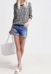 Haut à manches longues noir et blanc à motifs, shorts en denim, sandales plates blanches et un grand sac tote blanc. Tenue simple et décontractée.