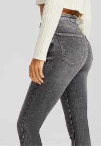 Vaqueros de denim gris de cintura alta con un corte ajustado, que cuentan con bolsillos traseros y ligeras variaciones de textura y desgaste.