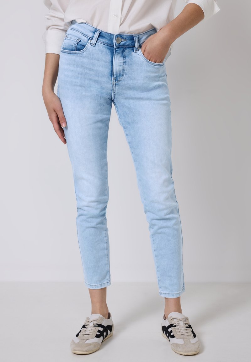 Jasnoniebieskie jeansy o slim fit, pięć kieszeni i zapięciem na guzik. Połączone z beżowymi i czarnymi trampkami.