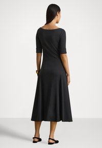 Melna ceļgalu garuma kleita ar trīs ceturtdaļu piedurknēm, plašu izgriezumu un izplešamu apakšu, izgatavota no mīksta, elastīga auduma. Vienkāršs dizains bez rakstiem.