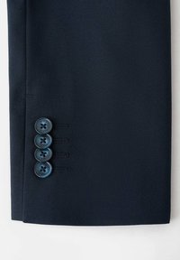 Pantaloni blu navy realizzati in tessuto morbido, con una vestibilità su misura, caratterizzati da quattro bottoni decorativi blu scuro lungo il polsino per la chiusura.