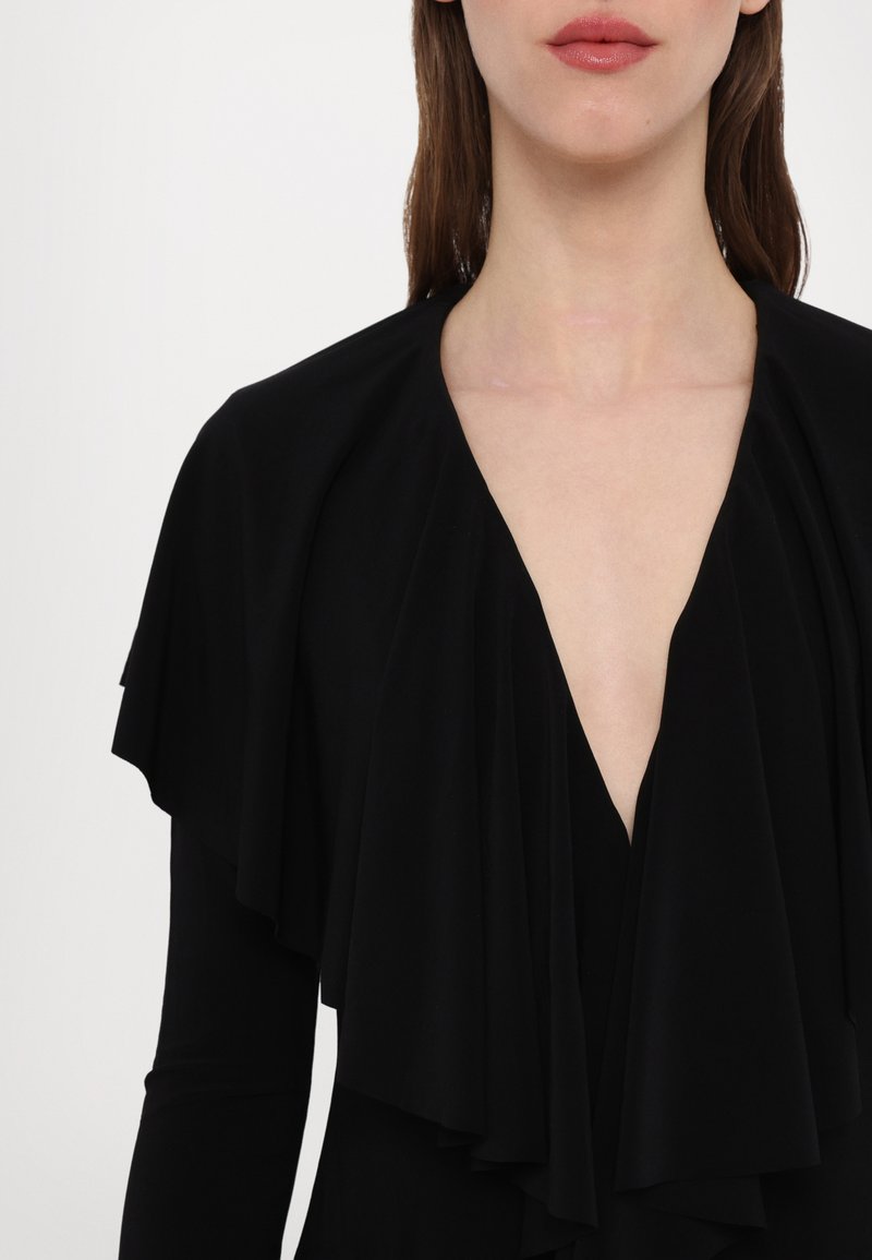 Zwarte jurk met gelaagd, hangend materiaal bij de halslijn en schouders. Diepe V-hals en een gladde textuur. Geen opvallende patronen of hardware.