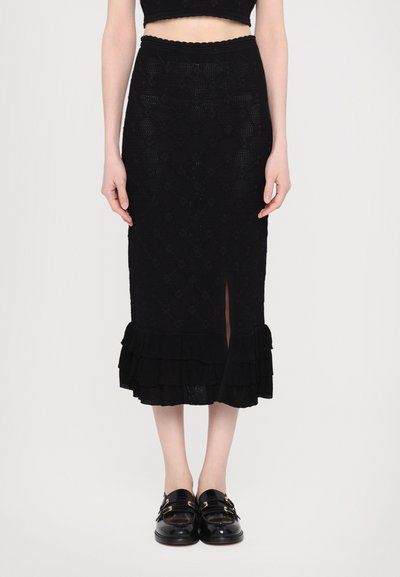 Sort strikket midi-nederdel med diamantmønster, volangkant og en frontslids. Kombineret med sorte loafers med guldhardware-accenter.