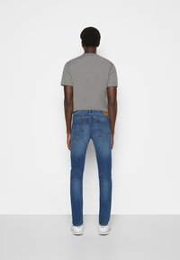 Camiseta gris de manga corta combinada con jeans ajustados azules, con un parche de logo en la cinturilla y un diseño clásico de 5 bolsillos.