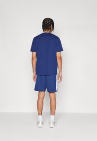 Navy blauwe t-shirt met korte mouwen in combinatie met bijpassende shorts met witte zijstrepen. De stof lijkt soepel en heeft een ontspannen pasvorm.