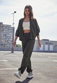 Groene sportoutfit met een cropped jack en bijpassende broek, gemaakt van zacht materiaal. Sneakers met een gestructureerd ontwerp in lichtgroen en wit.