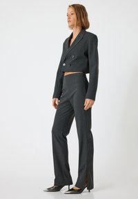 Grijze cropped dubbelknop blazer met grote knopen, gecombineerd met op maat gemaakte broek met zijsplitten en een gladde textuur. Zwarte spitse schoenen.