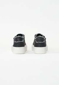 Mustad denimsneakerid rebenenud servadega, valged kummitaldad ja lihtne nööpimise disain. Tagapoolne vaade näitab minimalismi stiili.