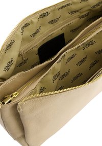 Beige Lederhandtasche mit strukturierter Oberfläche, ausgestattet mit zwei Reißverschlussfächern und einem mit hellbeigem Logo bedruckten Innenfutter.