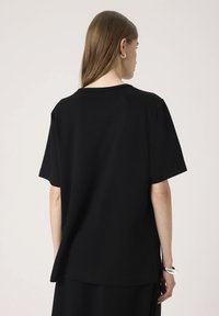 Sort t-shirt lavet af blødt bomuld, med løst fit, korte ærmer og rund halsudskæring. Inkluderer sideskår for ekstra detalje.