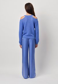 Blauer Strickpullover mit Schulterauschnitten, kombiniert mit hellblauen, weiten Satin-Hosen, zeichnet sich durch weiche Texturen und lässige Formen aus.