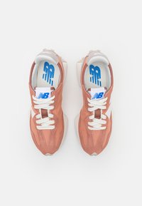 Růžové semišové tenisky s bílými akcenty, texturovaný svršek, silné bílé tkaničky a polstrovaná podešev. Obsahují logo na jazyku a design vnitřní sole.