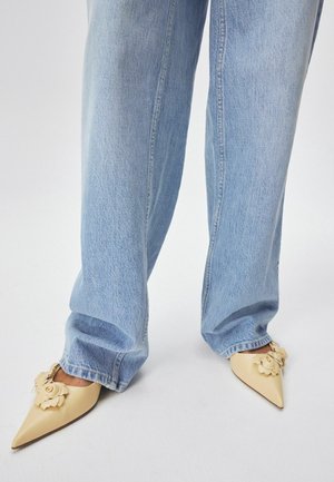 Beige puntige hakken met bloemdecoraties; gemaakt van glad leer. Draag ze met lichtblauwe wijde jeans.