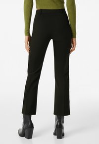 Svarta skräddarsydda byxor med rak benlösning, med en slät yta och sidfickor, tillsammans med svarta klackade ankelstövlar.