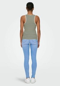 Canottiera a righe verde e bianca, design aderente, abbinata a jeans skinny azzurri chiari e sneakers bianche. Texture del tessuto liscia.