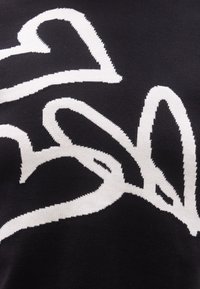 Μαύρο ύφασμα με λευκά αφηρημένα σχήματα καρδιάς και φύλλου πλεγμένα στο υλικό.