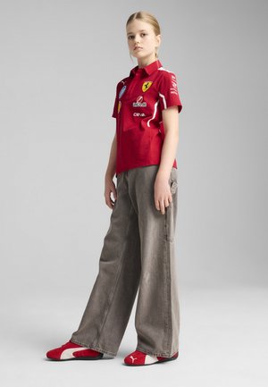 Rode poloshirt met Ferrari-branding, grijze wijde broek en rode schoenen. Minimalistisch ontwerp, zachte textuur, met logo- en patchdetails.
