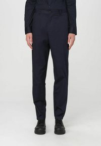 Pantaloni dritti blu navy in tessuto leggero con una texture liscia; dotati di chiusura con bottone e tasche frontali. Scarpe nere indossate.
