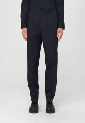 Pantaloni dritti blu navy in tessuto leggero con una texture liscia; dotati di chiusura con bottone e tasche frontali. Scarpe nere indossate.