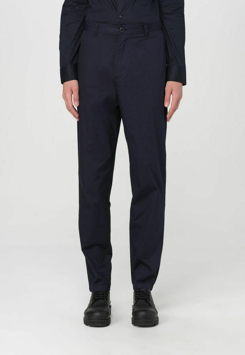 Pantaloni dritti blu navy in tessuto leggero con una texture liscia; dotati di chiusura con bottone e tasche frontali. Scarpe nere indossate.