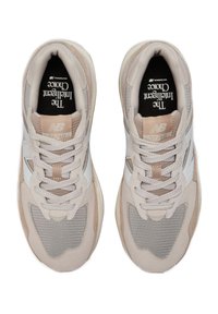Beige Sport Sneakers aus Mesh- und Wildledermaterialien, geschichtetes Design, flache Schnürung und weiße Logoakzente an den Seiten.
