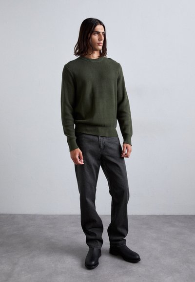 Dark green knitted sweater with ribbed cuffs and hem, paired with loose-fitting dark gray jeans and black ankle boots. Simple design.