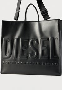 Μαύρη ορθογώνια δερμάτινη τσάντα χειρός με διπλές λαβές και λουρί ώμου, με ανάγλυφο λογότυπο "DIESEL FOR SUCCESSFUL LIVING" στην πρόσοψη.