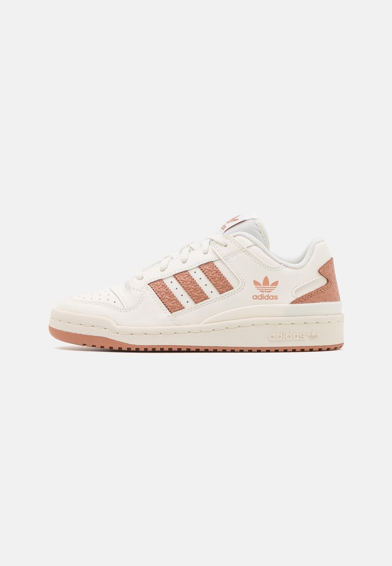Baskets basses blanches Adidas avec des bandes marron clair et un détail au talon, bout perforé et semelle à logo sur un fond uni.