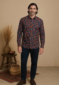 Langarm overhemd met een donkerblauw en oranje bloemenpatroon. Gemaakt van stof met een gladde textuur; gecombineerd met marineblauwe broek.