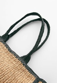 Tan geweven rieten tas met zwarte gevlochten handvatten, met een gestructureerd oppervlak en contrasterende kleuren, geschikt voor casual gebruik.