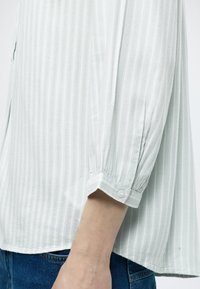 Ανοιχτό πράσινο μπλουζάκι με κάθετες ρίγες, ελαφρύ ύφασμα, μανίκια 3/4 μήκους και λεπτομέρεια με κουμπιά στα μανίκια. Λεπτή υφή και άνετη εφαρμογή.