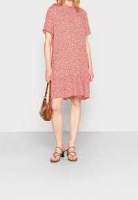 Robes rouge à fleurs à manches courtes avec une coupe ample et un ourlet à volants, associées à des sandales marron à lanières et un petit sac à main marron à motif.