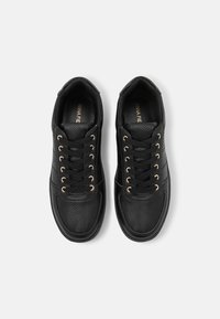 Black sneakers made of textured material with smooth accents. Features gold-tone eyelets, round laces, and a padded collar.