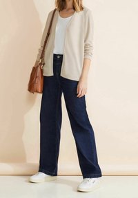 Beige kofta, vit topp, mörkblå vida jeans och vita sneakers. Brun handväska, slätt tyg, avslappnad passform och casual design.