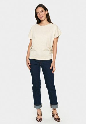 Haut beige à manches courtes avec une coupe décontractée, associé à un jean bleu foncé à ourlets et des chaussures à talons carrés à motifs. Design simple et décontracté.