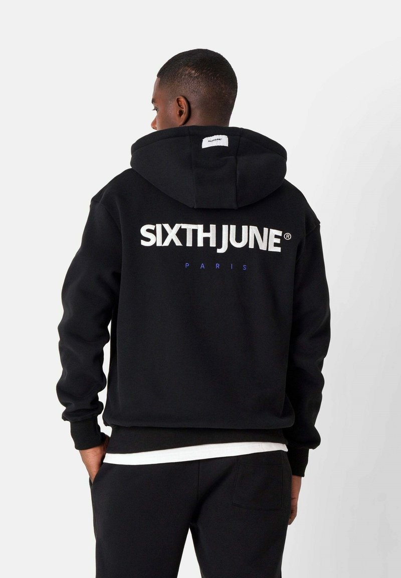 Sudadera negra con el texto "SIXTHJUNE" en grandes letras blancas y "PARIS" en texto pequeño azul. Material de algodón con un corte relajado y capucha ajustable.