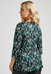 Maglietta a maniche lunghe con un motivo astratto in nero, teal e bianco. Il tessuto ha una texture setosa, con una vestibilità rilassata e un leggero drappeggio.