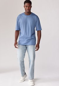Blå bomulds T-shirt med afslappet pasform, rund hals og korte ærmer, parret med falmede lyseblå jeans og hvide sneakers.