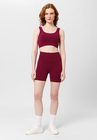 Bordeaux sportieve crop top en hoge taille shorts gemaakt van rekbare stof. Het model draagt witte sneakers en crew-sokken.
