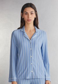 Blauwe gestreepte pyjamaspijker met lange mouwen, met een notch-kraag, knoopsluiting en witte accenten langs de randen. Glad stofoppervlak.