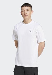 Bílý bavlněný tričko s kulatým výstřihem a krátkými rukávy. Na levé hrudi se nachází malé černé logo Adidas. Jednoduchý a solidní design.
