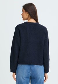 Maglione navy a maglia con texture a coste, spalle cadenti e design cropped. Caratterizzato da un collo rotondo e maniche lunghe.