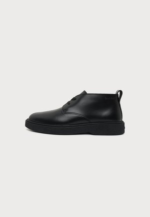 Black leather ankle boot with thick sole and two eyelets for laces, side stitching, and pull tab at the back.